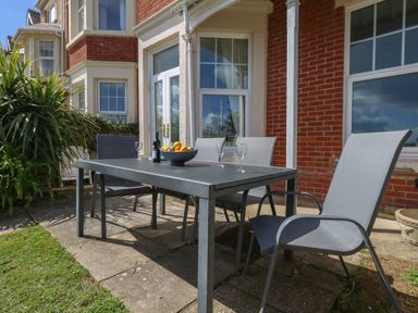 An outdoor patio with a gray table and four chairs next to a brick house with French doors and windows with curtains at Blue Yonder in Weymouth