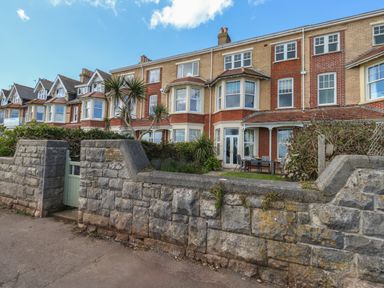 A row of brick townhouses with bay windows behind a stone wall and a small green gate at Blue Yonder in Weymouth