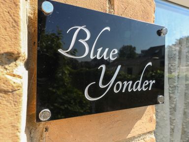 A black plaque with the words Blue Yonder mounted on a brick wall near a window at Blue Yonder in Weymouth