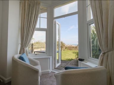 A seating area with two armchairs and blue cushions near windows and a door opening to a garden at Blue Yonder in Weymouth