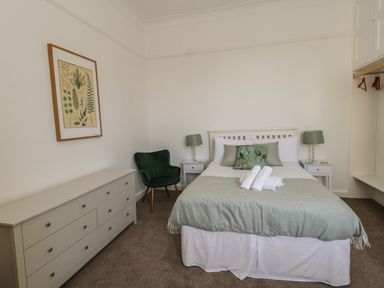A bedroom with a double bed with green and white bedding a green armchair two white bedside tables with lamps a white dresser and a framed botanical print on the wall at Blue Yonder in Weymouth