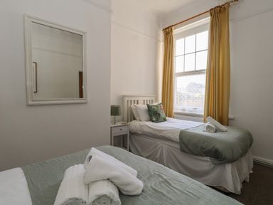 A bedroom with two single beds a bedside table with a lamp a window with yellow curtains and a wall mirror at Blue Yonder in Weymouth