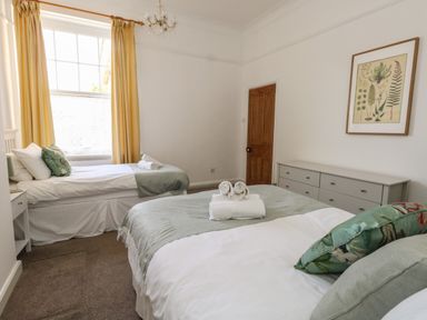 A bedroom with two beds a dresser a wooden door and a window with yellow curtains at Blue Yonder in Weymouth