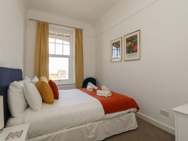 A bedroom with a bed with orange and yellow cushions and framed pictures on the wall at Blue Yonder in Weymouth