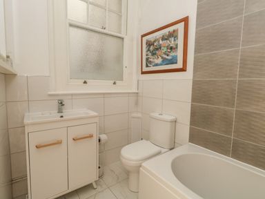 A bathroom with a sink cabinet, toilet, bathtub, and a framed picture on the wall at Blue Yonder in Weymouth