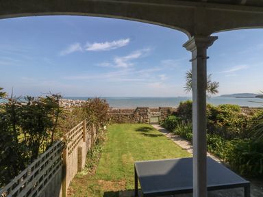 A garden with grass and plants overlooking the sea from a covered patio at Blue Yonder in Weymouth