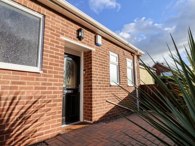 The exterior of a brick house with a black door and three windows beside a paved pathway at Meadowfields in Whitby