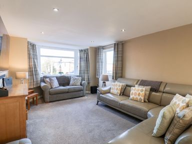 A living room with two sofas a wooden cabinet lamps and plaid curtains at Meadowfields in Whitby