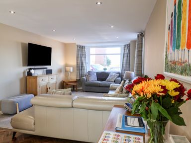 A living room with sofas a wall mounted TV and a vase of flowers on a table at Meadowfields in Whitby