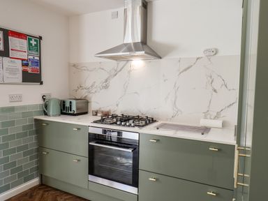 A kitchen with green cabinets a stove oven stainless steel hood toaster kettle and notice board at Meadowfields in Whitby