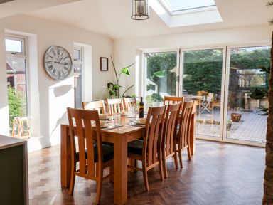 A dining room with a wooden table and eight chairs set with plates and glasses next to large sliding glass doors at Meadowfields in Whitby