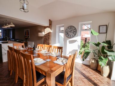 A dining room with a wooden table set for a meal a large clock on the wall and plants in pots at Meadowfields in Whitby
