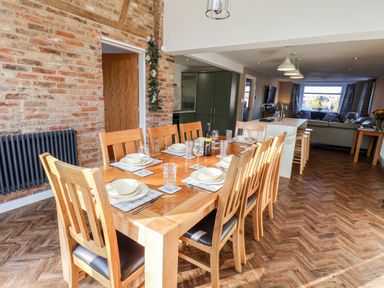 A dining area with a wooden table set for eight people next to an open kitchen and living room at Meadowfields in Whitby
