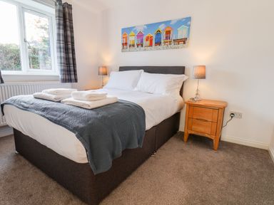 A bedroom with a double bed white linens bedside table with lamp and window at Meadowfields in Whitby