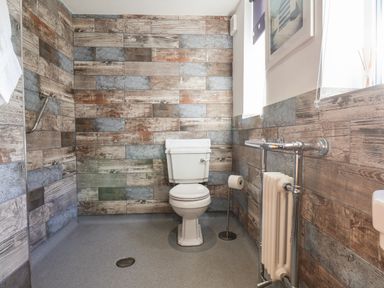 A bathroom with a white toilet a metal toilet paper holder a radiator and walls covered with multicolored wood paneling at Meadowfields in Whitby