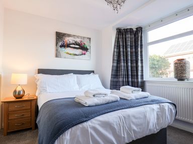 A bedroom with a bed folded towels on a blue blanket a bedside table with a lamp and a window with curtains at Meadowfields in Whitby