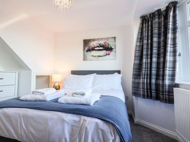 A bedroom with a bed folded towels bedside lamp chest of drawers and a window with plaid curtains at Meadowfields in Whitby