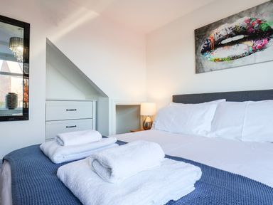 A bedroom with a bed made with white sheets and towels on a blue blanket with a chest of drawers mirror and lamp at Meadowfields Whitby