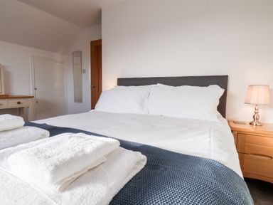 A bedroom with a bed with white sheets towels on a blue blanket and a wooden nightstand with a lamp at Meadowfields in Whitby