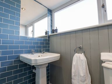 A bathroom with a pedestal sink a mirror blue tiled wall a window and a white towel at Meadowfields in Whitby