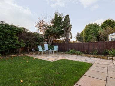 A backyard with grass a paved seating area with three chairs and plants along a wooden fence at Meadowfields in Whitby