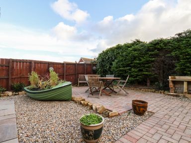 An outdoor patio with wooden chairs and table a green boat planter and potted plants at Meadowfields in Whitby