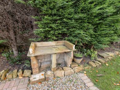 An outdoor stone bench with a planter next to it surrounded by gravel and greenery at Meadowfields in Whitby