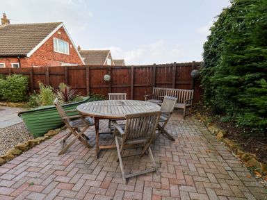 An outdoor patio with a wooden round table and chairs near a wooden bench and a green planter at Meadowfields Whitby