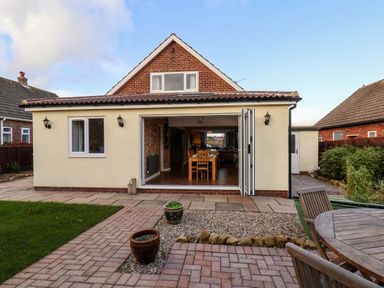 The back of a house with an open folding door leading to a dining area and a backyard with patio furniture and potted plants at Meadowfields in Whitby