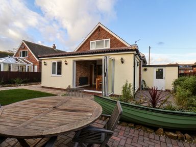 A backyard with wooden outdoor table and chairs next to a house with folding glass doors open at Meadowfields in Whitby