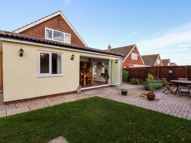 A backyard with a lawn patio dining table and chairs and a house with an open folding door at Meadowfields in Whitby