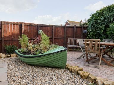 A garden with a green boat planter filled with plants next to a wooden table and chairs at Meadowfields Whitby