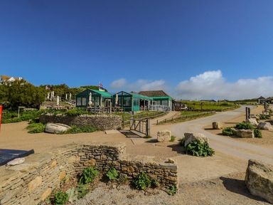 An outdoor dining area with green canopy tents and a dirt road surrounded by stone walls and rocks at Alice's Cottage in Burton Bradstock