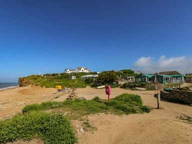 A coastal area with a sandy beach picnic tables and buildings under a clear blue sky at Alices Cottage in Burton Bradstock