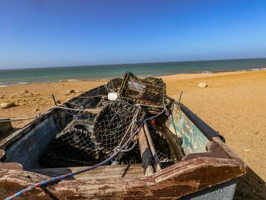 A boat with fishing nets and ropes on a sandy beach with the sea and clear sky in the background