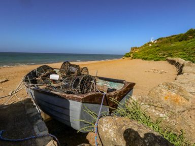 A small fishing boat with lobster pots on a sandy beach near the sea with grassy cliffs in the background at Alice's Cottage in Burton Bradstock