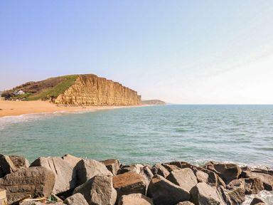 A rocky shoreline with cliffs and a sandy beach by the sea at Alices Cottage in Burton Bradstock