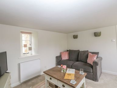 A sitting room with a grey sofa and pink cushions next to a wooden coffee table and a television at Alice's Cottage in Burton Bradstock