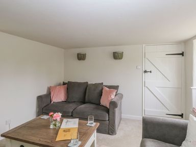 A sitting room with a grey sofa with pink cushions wooden coffee table and a white door at Alices Cottage in Burton Bradstock