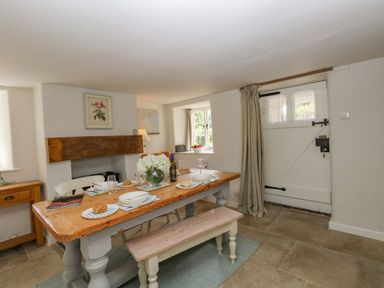 A dining room with a wooden table set for four near a white door and a window at Alices Cottage in Burton Bradstock