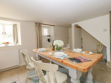 A dining room with a wooden table set with plates glasses and a bottle of wine at Alice's Cottage in Burton Bradstock