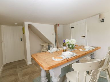 A dining room with a wooden table set for four people white chairs and a vase with flowers at Alices Cottage in Burton Bradstock