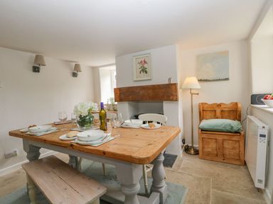 A dining room with a wooden table set for four near a fireplace and wooden bench at Alices Cottage in Burton Bradstock