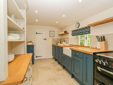 A kitchen with wooden countertops blue cabinets a white sink and a black stove at Alices Cottage in Burton Bradstock
