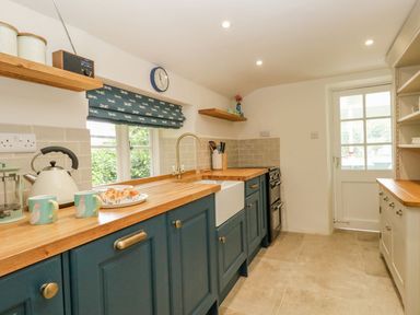 A kitchen with blue cabinets wooden countertops a white farmhouse sink and a door with window panes at Alices Cottage in Burton Bradstock