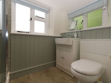 A bathroom with a toilet sink cabinet a mirror and windows at Alices Cottage in Burton Bradstock