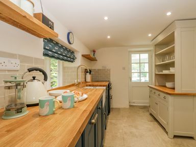 A kitchen with wooden countertops blue and white cabinets shelves and a door at Alices Cottage in Burton Bradstock