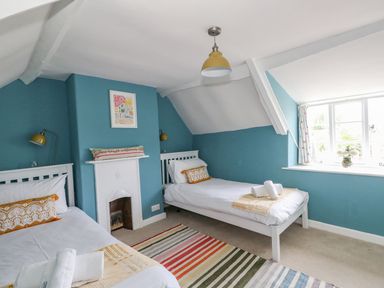 A bedroom with two single beds a window and a small fireplace at Alices Cottage in Burton Bradstock