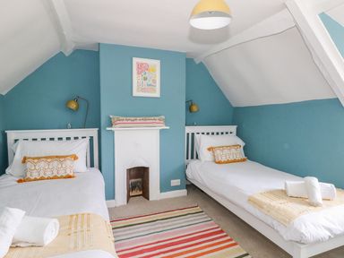 A bedroom with two single beds a striped rug and a small fireplace at Alices Cottage in Burton Bradstock