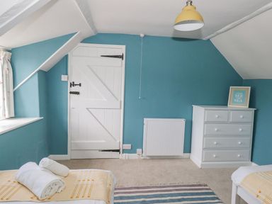 A bedroom with blue walls a white door a white dresser folded towels on beds and a striped rug at Alices Cottage in Burton Bradstock